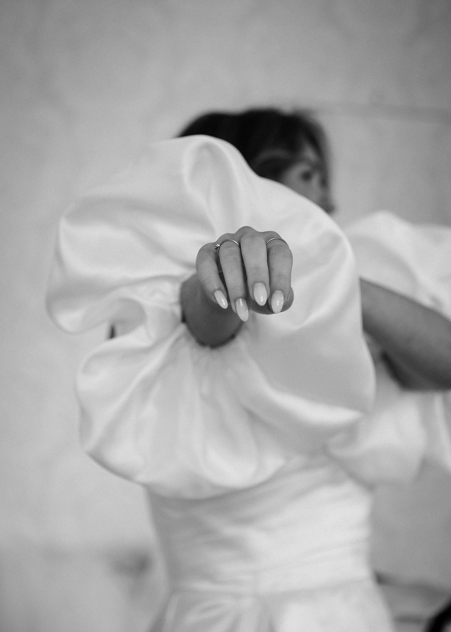 Close-up black and white photo of hands adjusting a white wedding dress fabric.