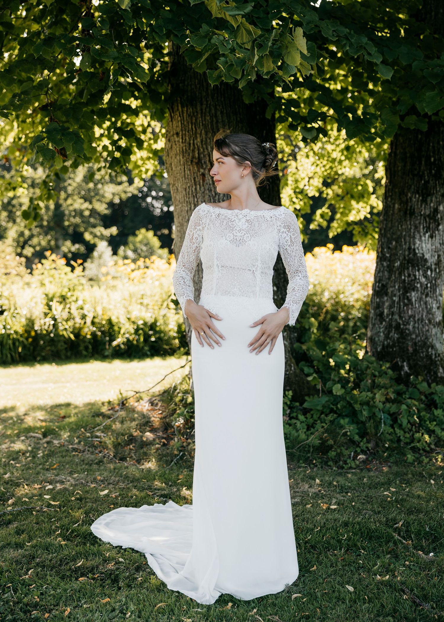 Elegant white wedding dress with lace details shown in garden setting.