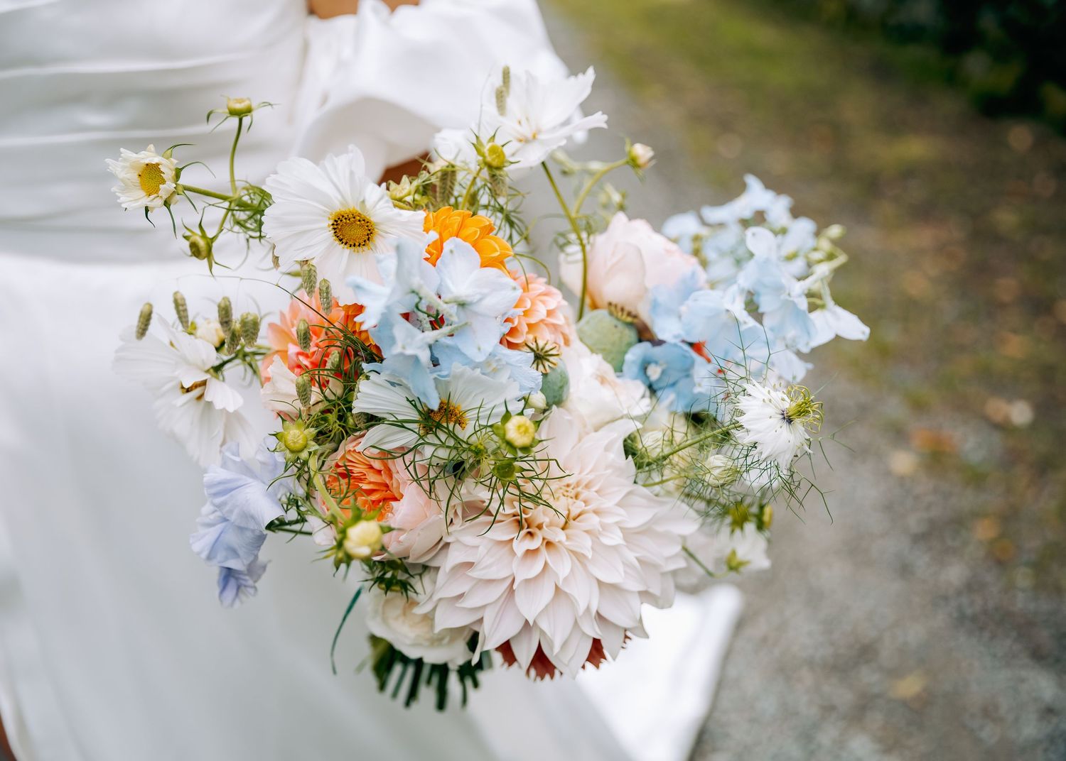 Delicate bridal bouquet with white daisies, pink dahlias and blue flowers against white fabric.