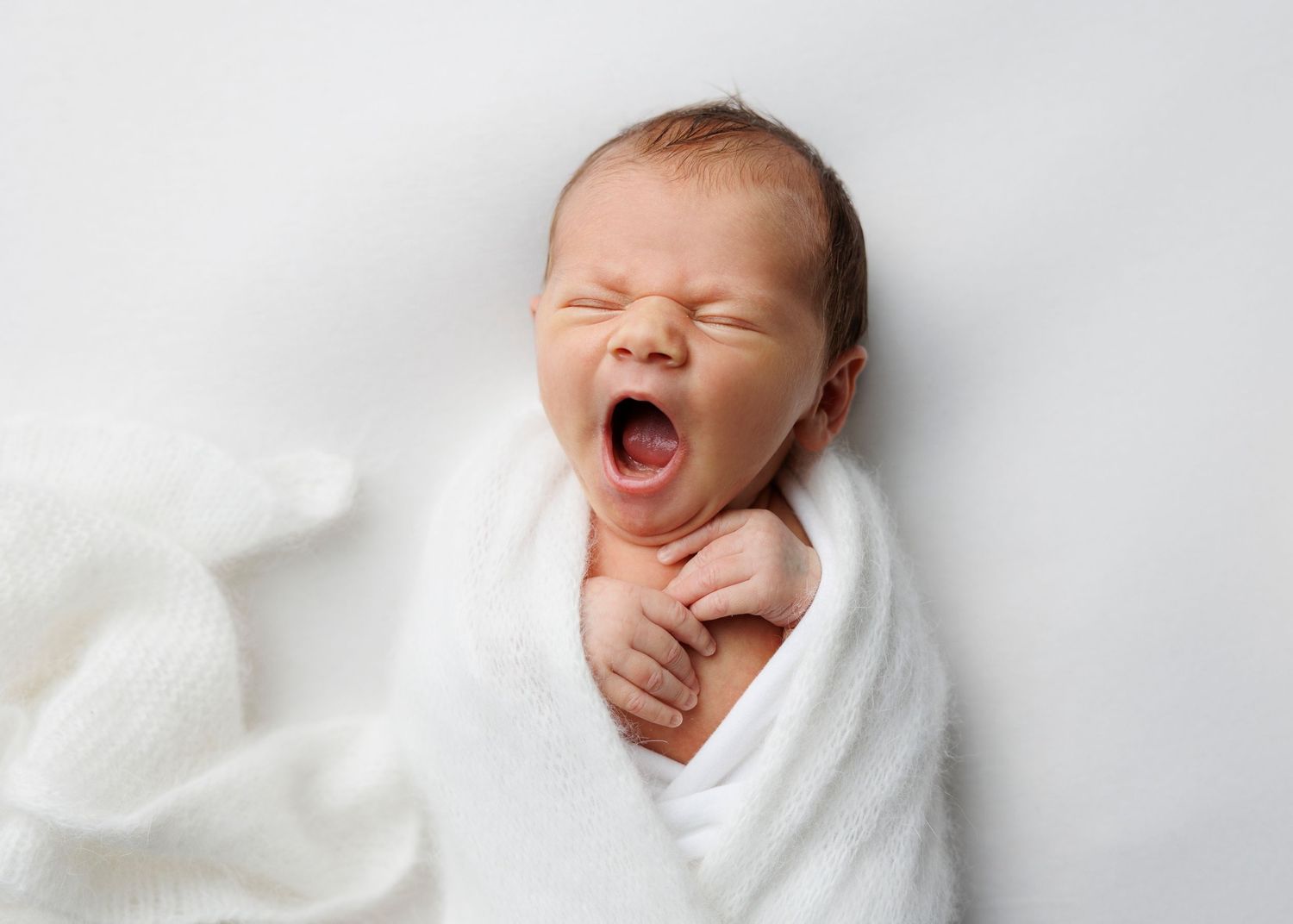 Series of newborn baby expressions while wrapped in white blanket against light background.