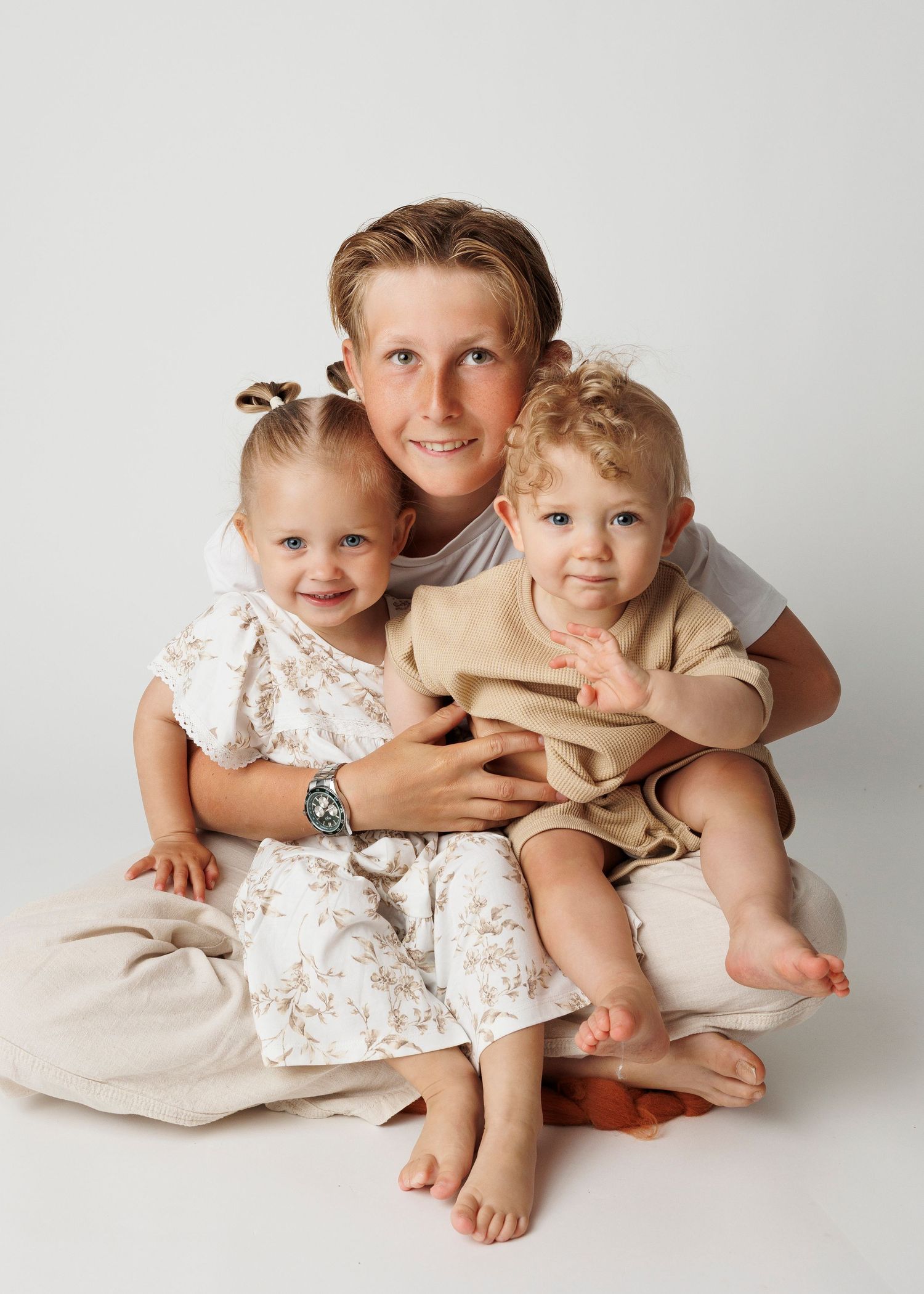 Children in light colored clothing sitting close together on white background for portrait.