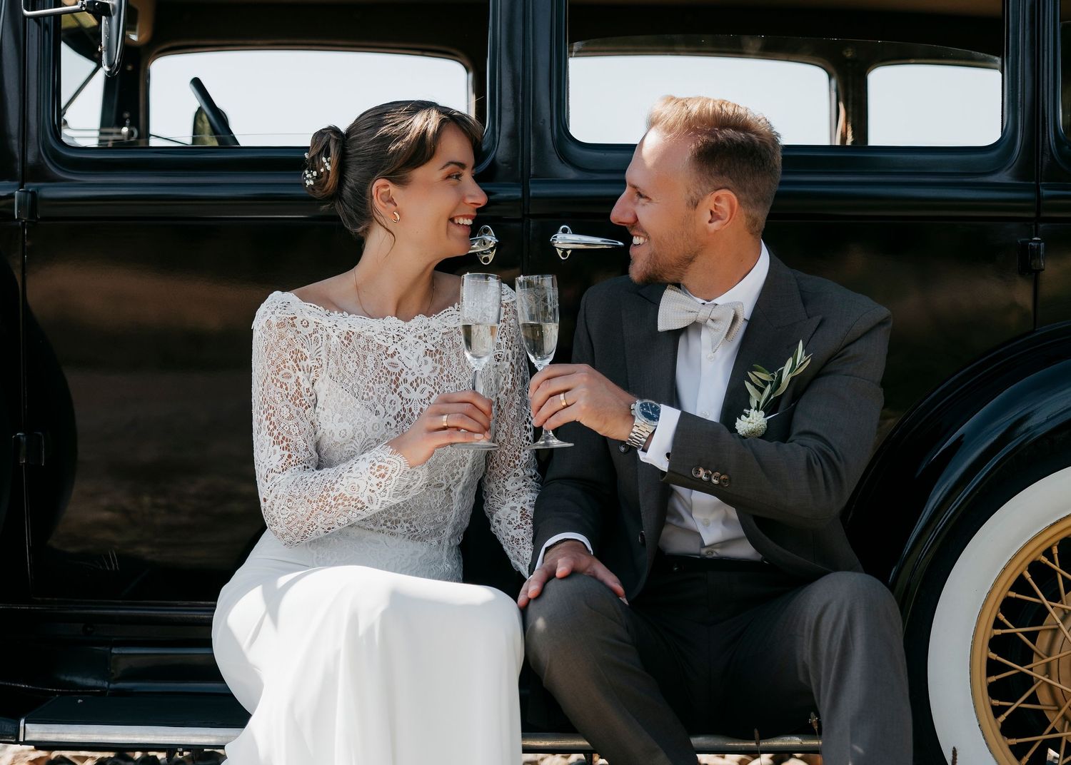 Classic black vintage car serves as backdrop for romantic wedding photos.