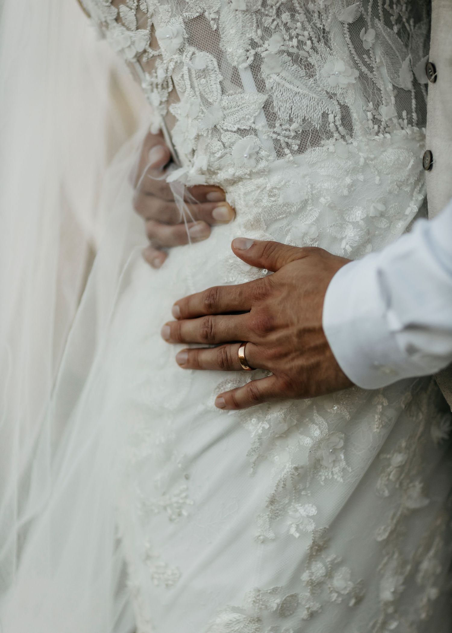 Close-up details of delicate lace on a white wedding dress with hands.