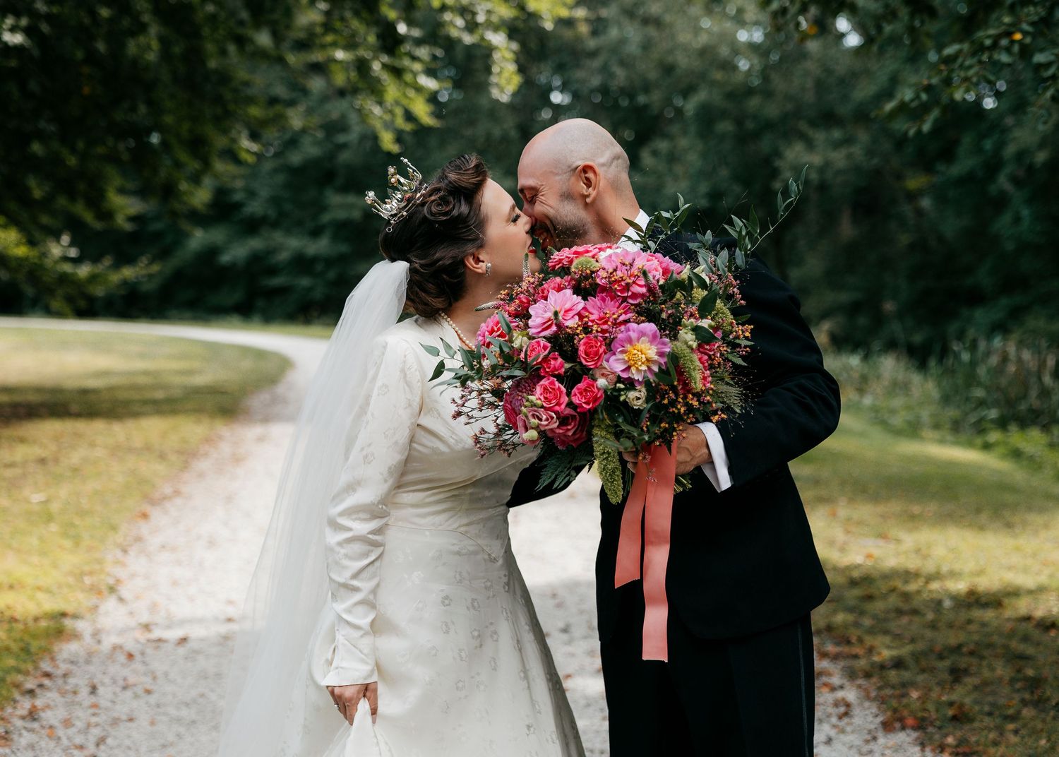 A romantic wedding couple shares intimate moments in a garden setting with pink floral bouquets and elegant attire.