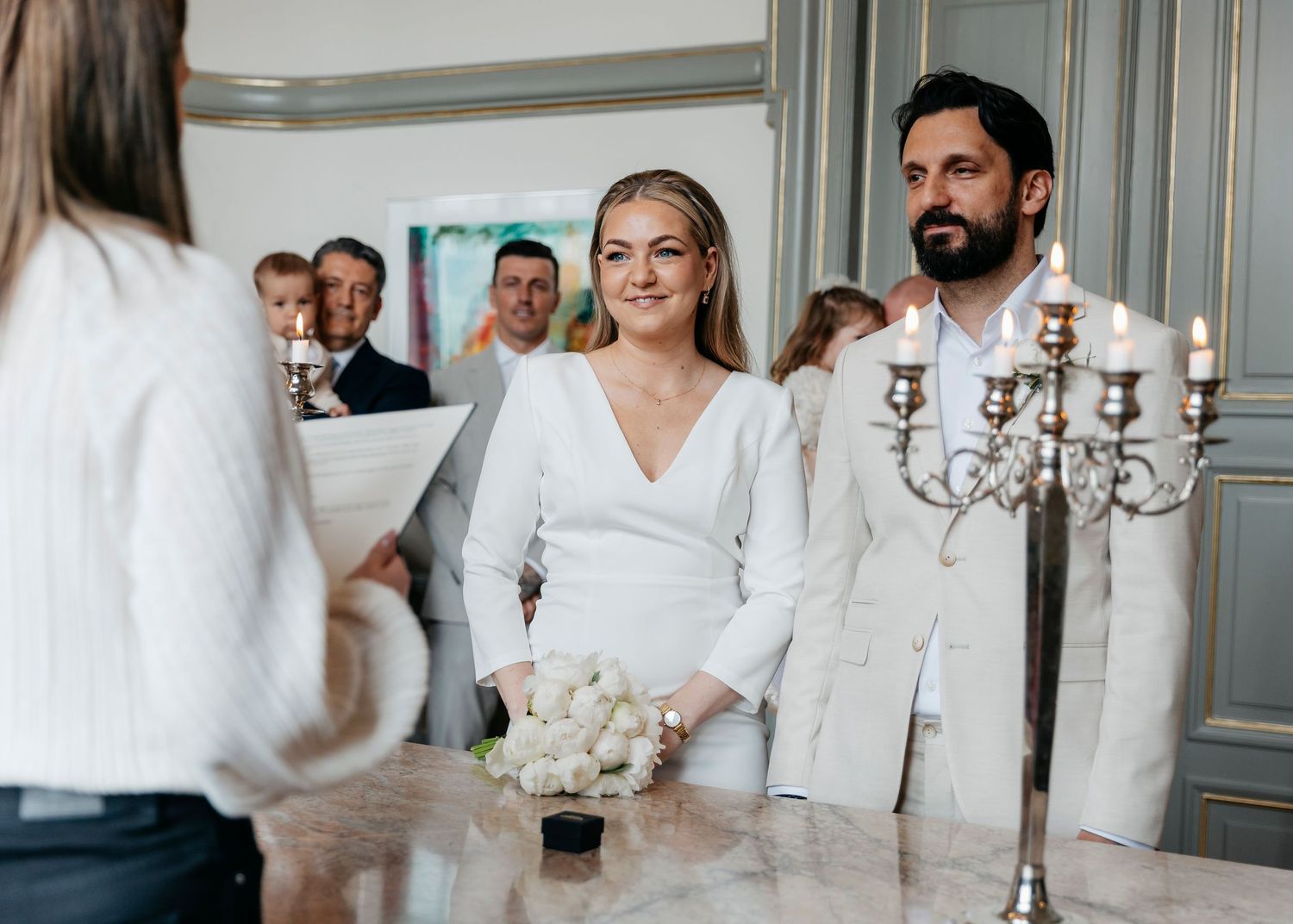 Wedding ceremony in an elegant room with gray walls and white-dressed attendees.