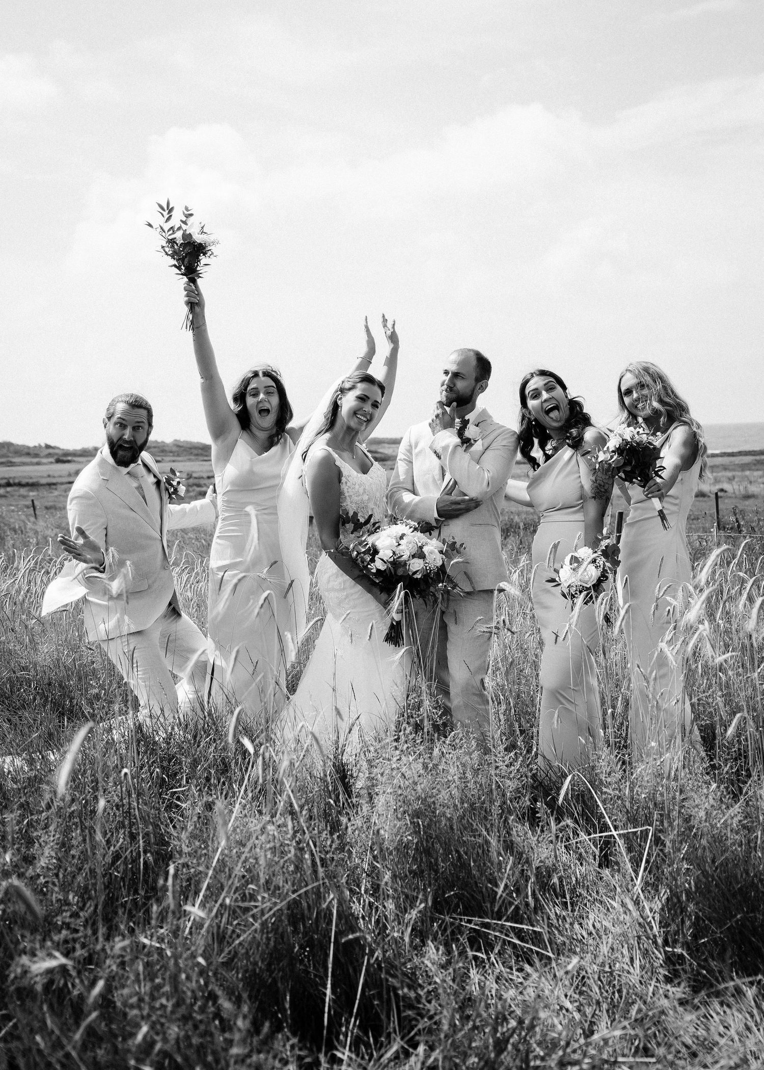 Joyful wedding party celebrating in a wheat field wearing white dresses.