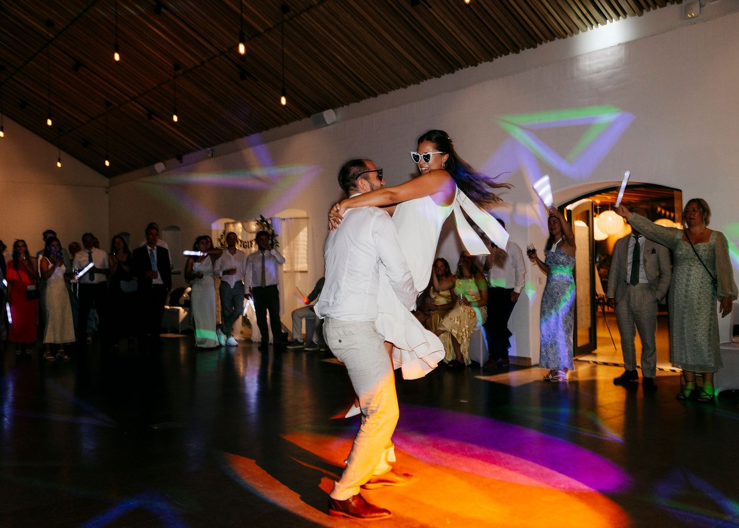 Couple dances on a rainbow-lit dance floor during their wedding reception.