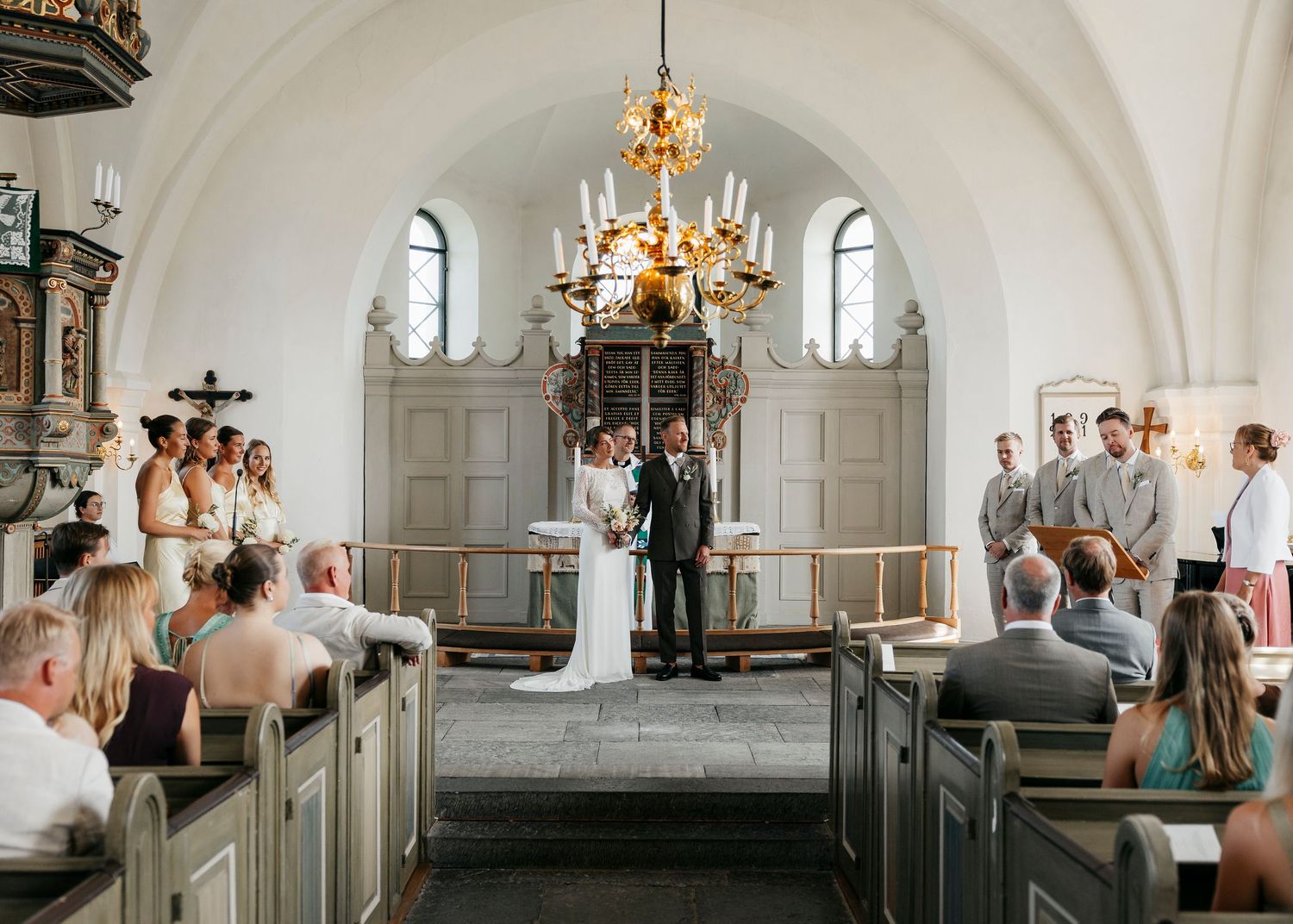 Traditional white church interior with arched ceilings and wooden pews during a ceremony.