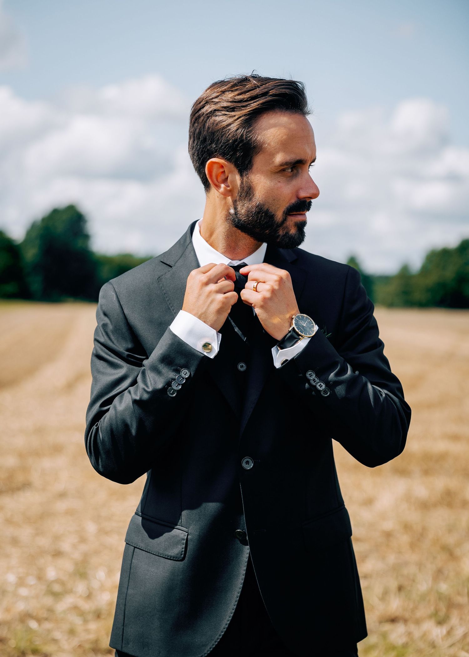 Wedding day emotional reactions captured in black suit against natural outdoor setting.