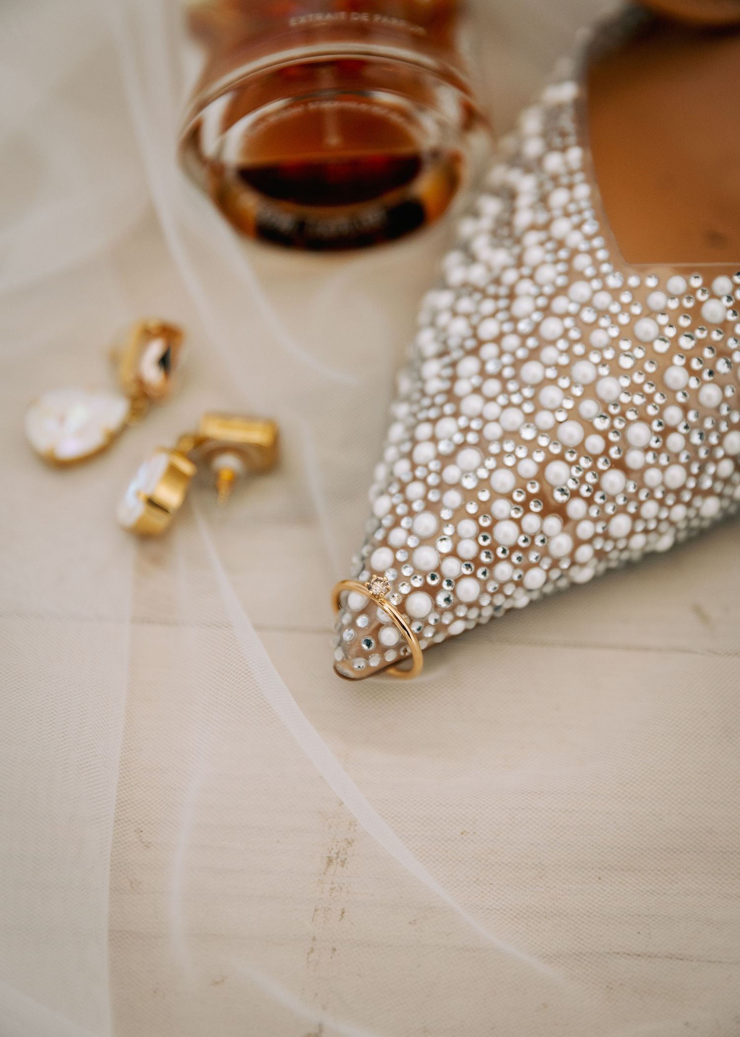 Wedding accessories including pearl shoes, rings and drink on light surface.
