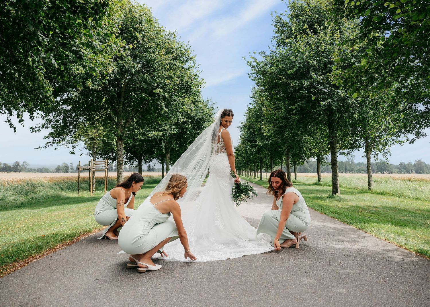Bride and groom share candid moments on scenic path with vintage car.