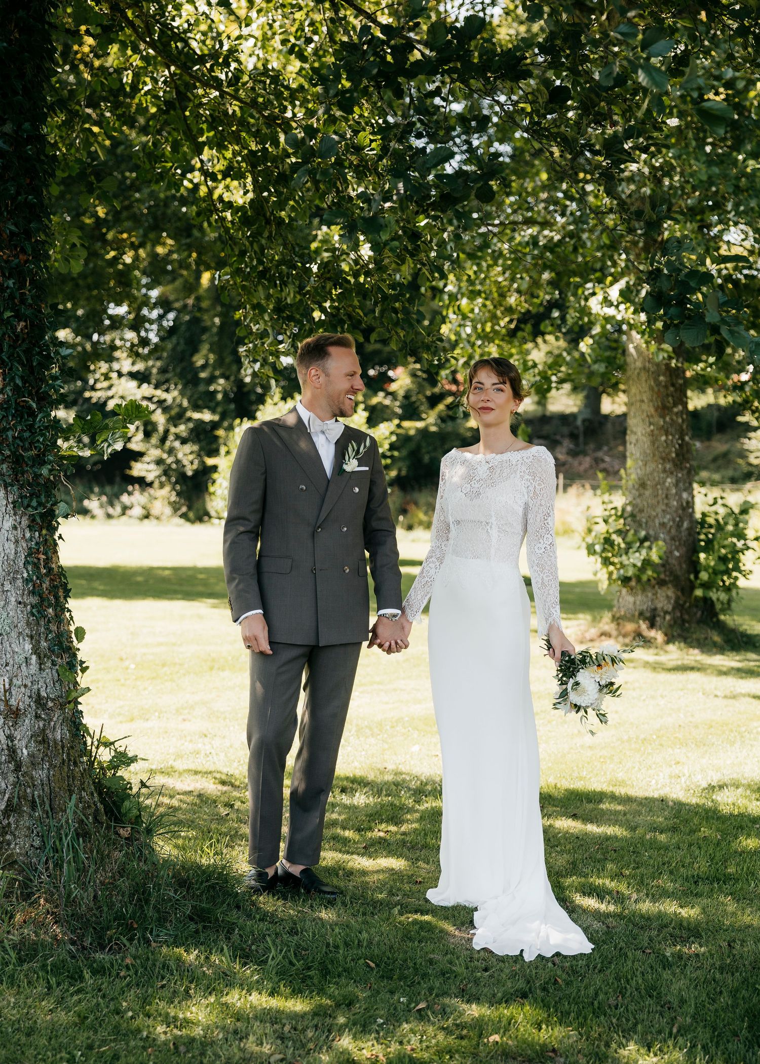 Wedding couple shares tender moments during outdoor photo session under shaded trees.