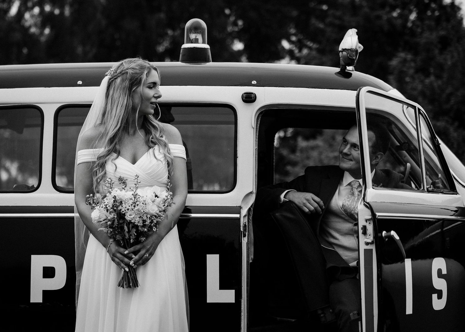 Vintage police car serves as backdrop for elegant wedding photo shoot in black and white.