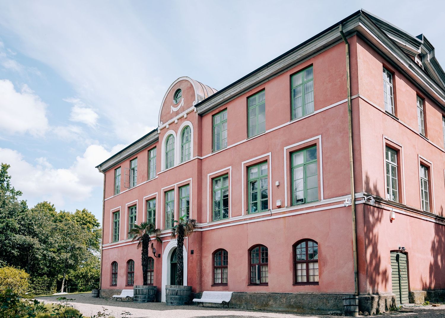 Pink historic mansion building with arched windows and ornate architectural details against blue sky.