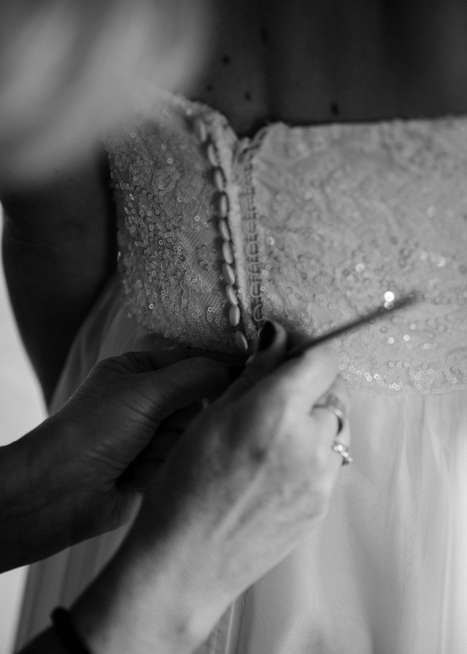 Close-up of hands adjusting delicate lace details on white wedding dress.
