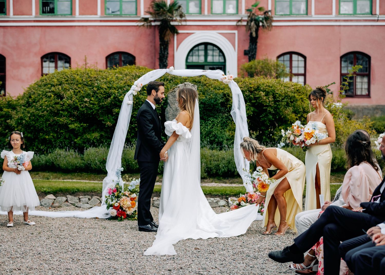 Wedding ceremony setup with white chairs and pink building facade featuring arched windows.
