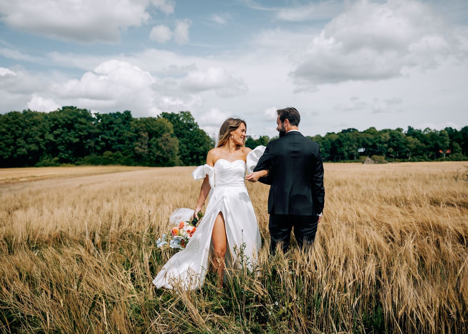 Romantic wedding couple holding hands in rustic wheat field.