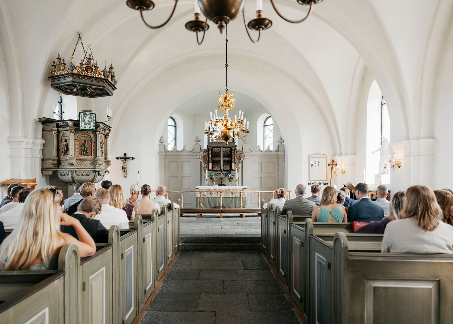 Interior of traditional white church with chandelier and wooden pews.