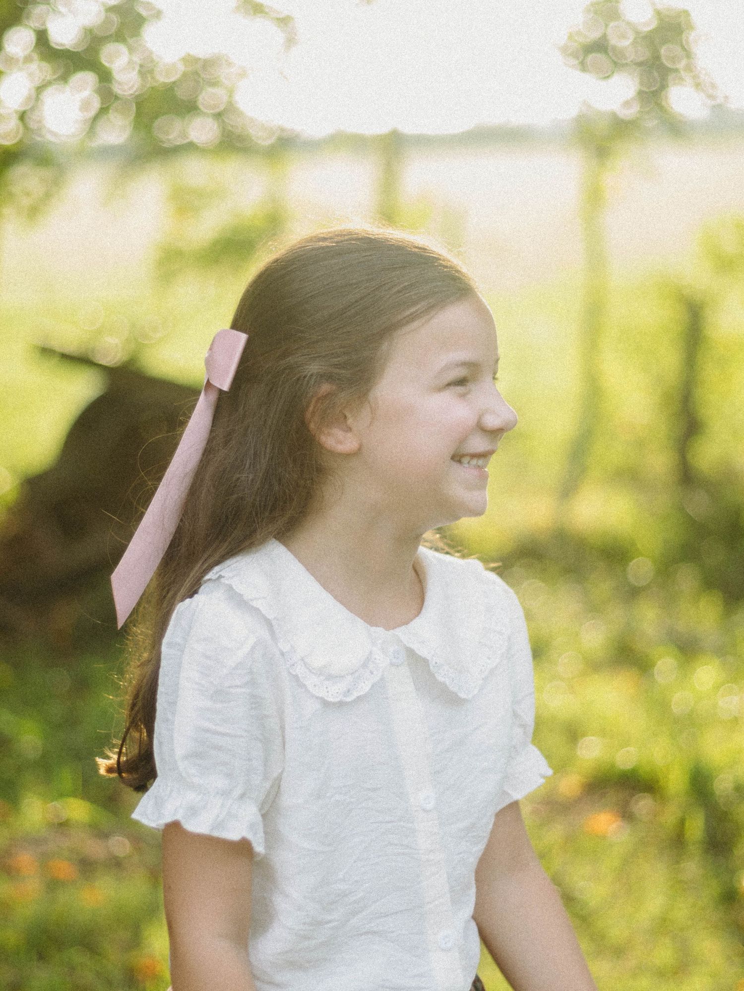 Child in white dress laughing joyfully in a sunlit garden setting.
