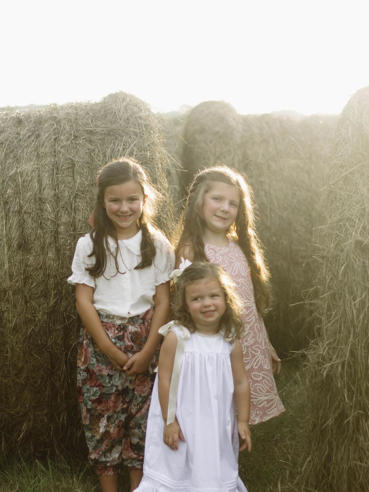 Children playing together in a sunlit field with hay bales in the background.