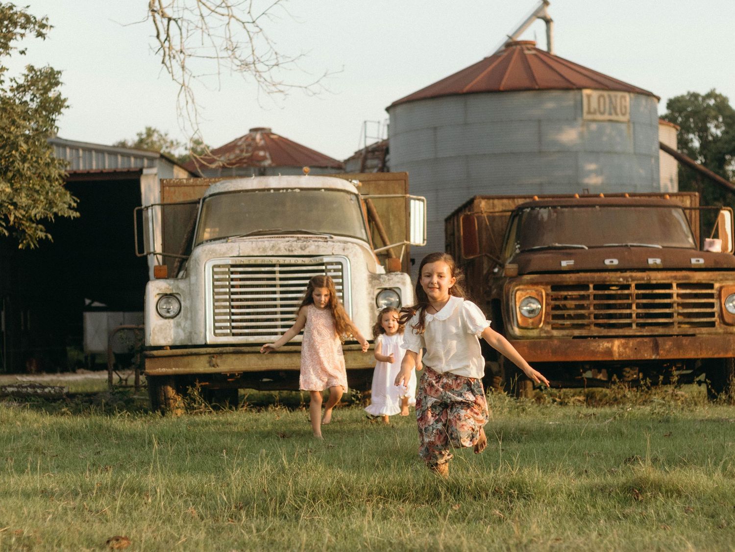 Rural farm setting with vintage trucks and grain silos at golden hour.