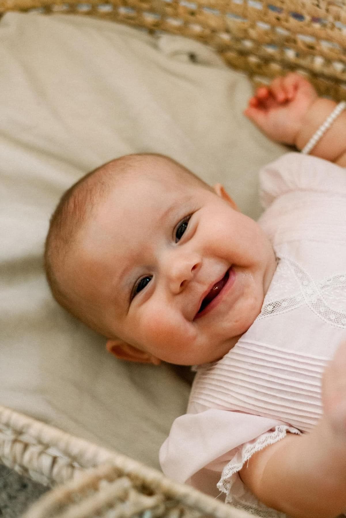 A smiling baby in white clothing lies on soft textured bedding.