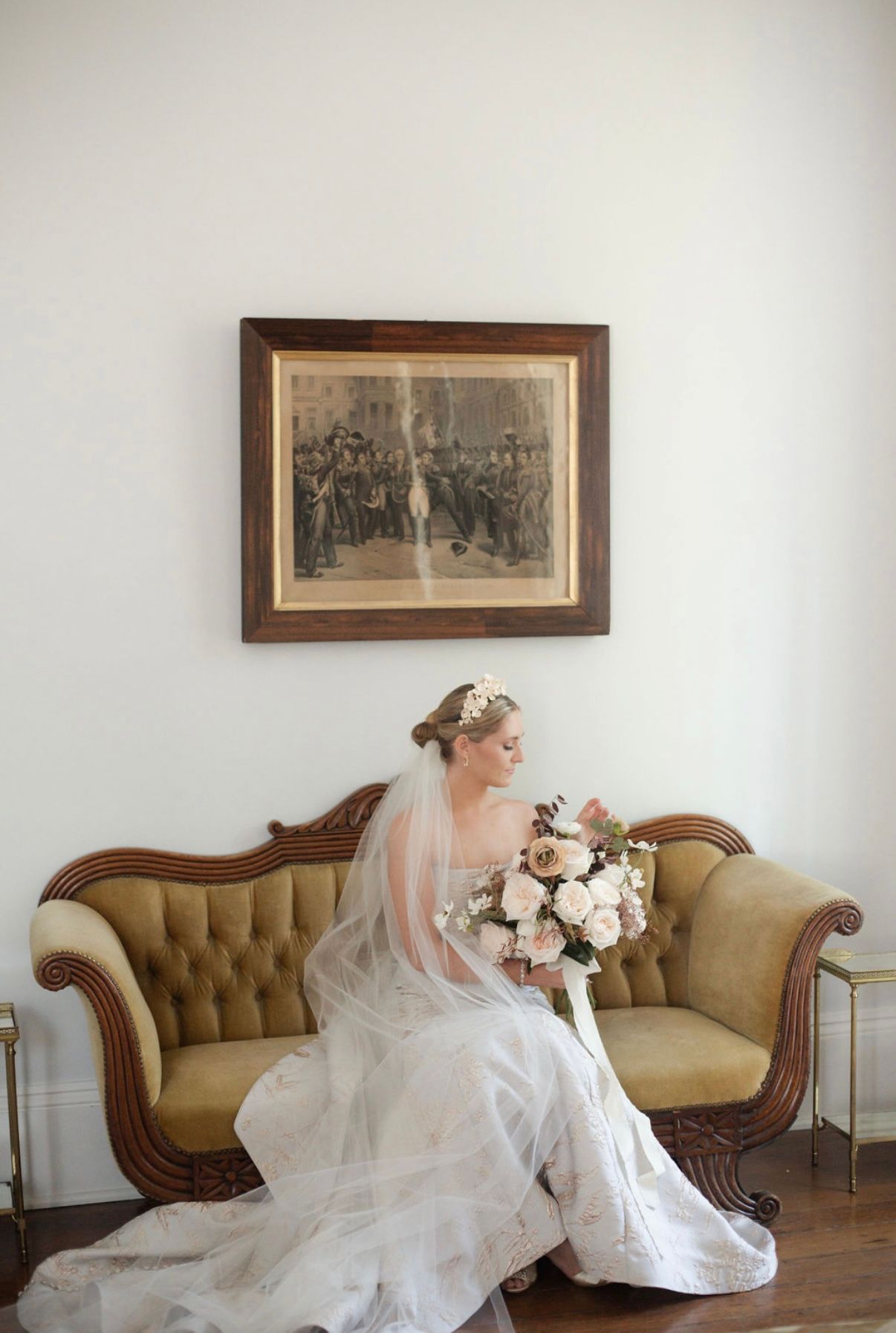 Elegant bridal portrait on vintage furniture against white walls with antique framed artwork.