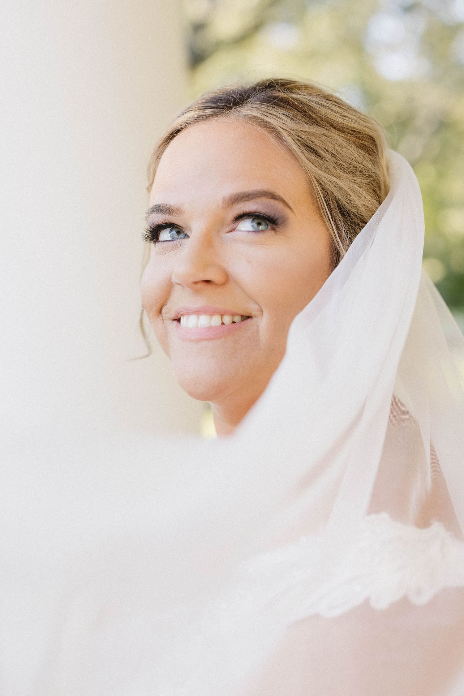 A bride wearing a white veil smiles radiantly in a series of close-up portraits against a soft, natural background.