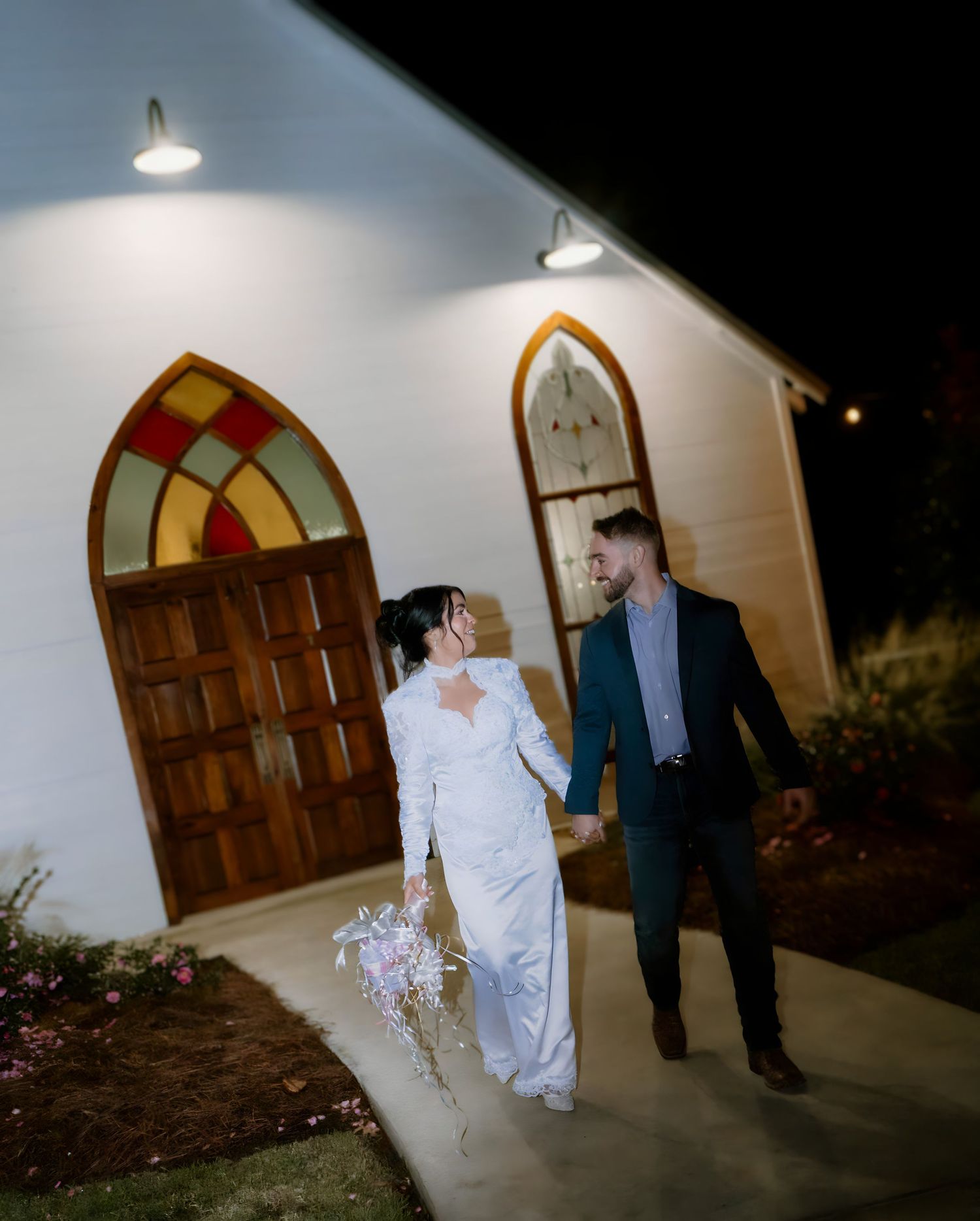 Dramatic nighttime scene outside wooden arched doors with spotlighting.