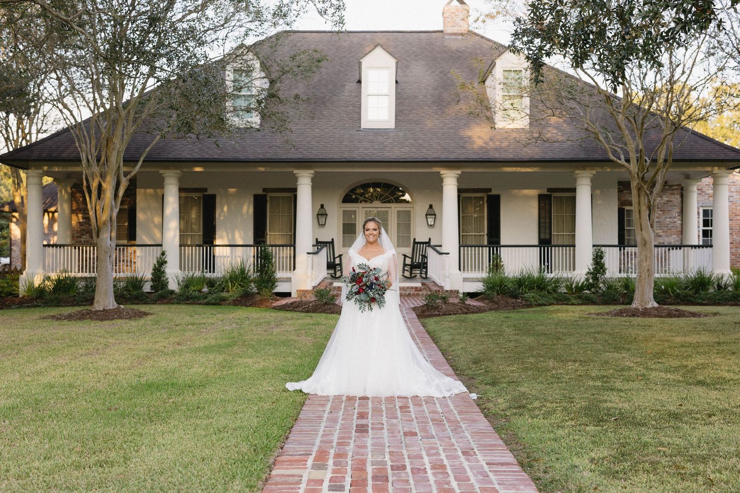 Historic white plantation house with brick walkway and wrap-around porch on a manicured lawn.