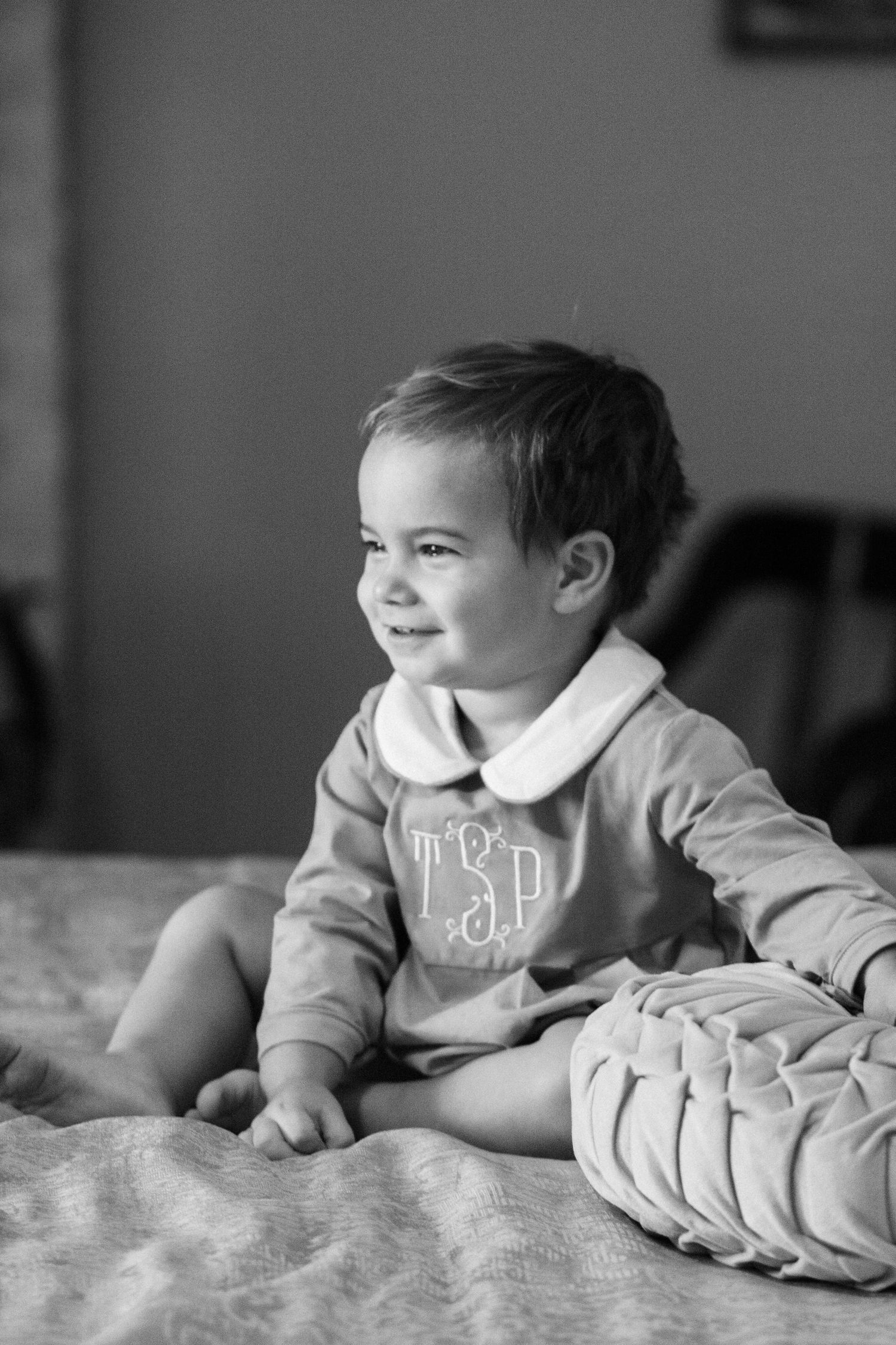 A black and white portrait of a smiling child wearing a monogrammed sweater.