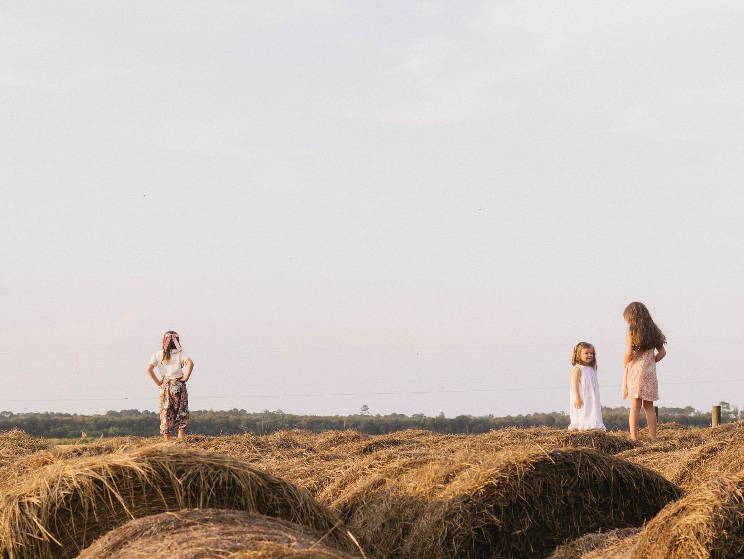 Silhouettes of people standing on hay bales against a sunset sky in a rural field.