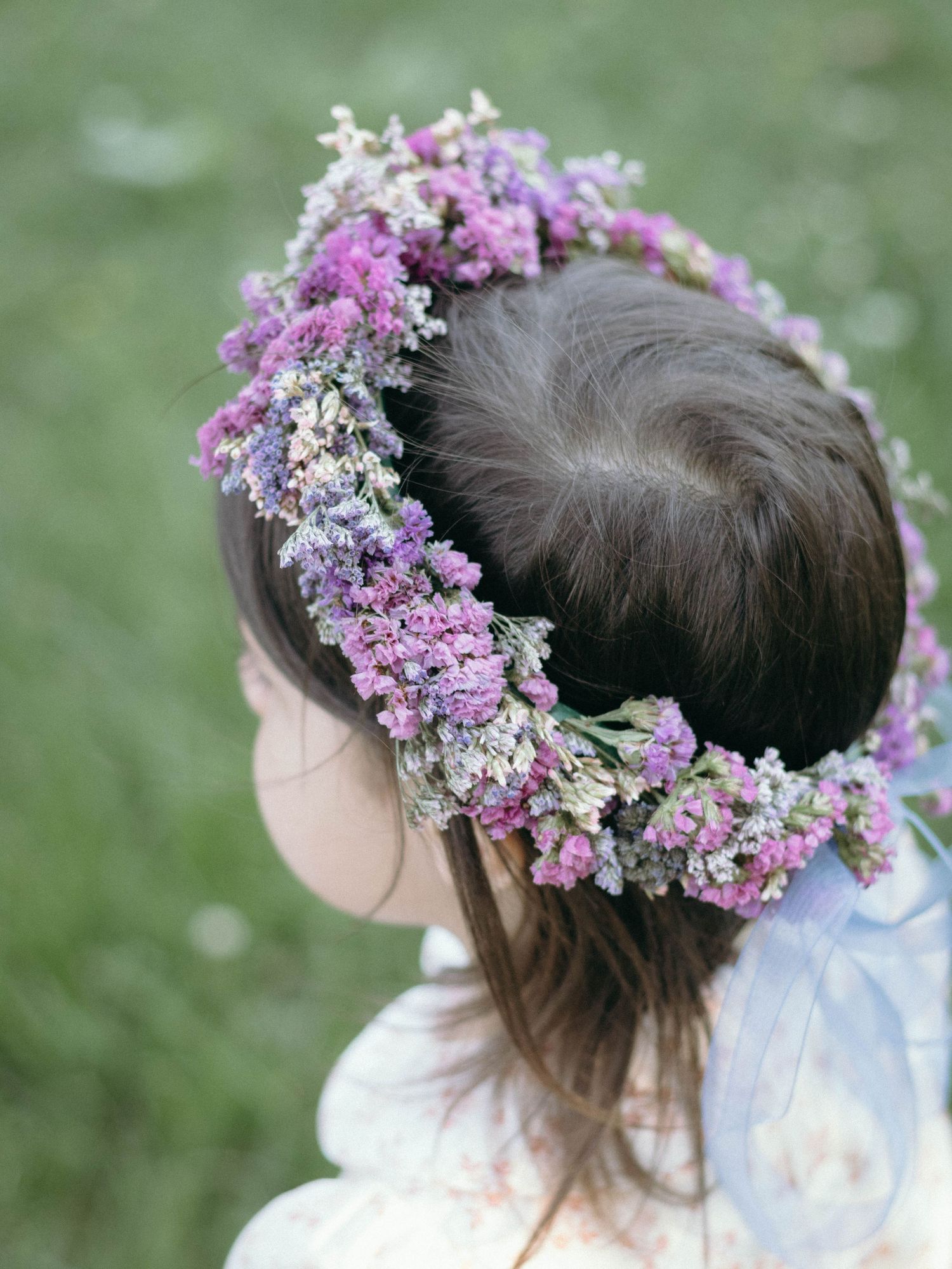 A delicate floral crown made of purple and white flowers adorns dark hair against a soft green background.