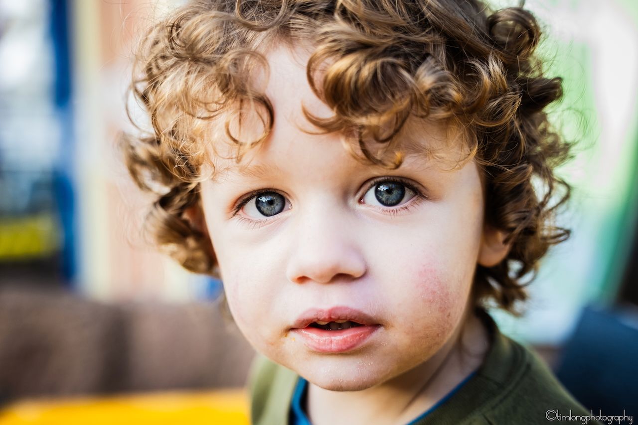 Close up portrait of a young child with curly hair and bright blue eyes.