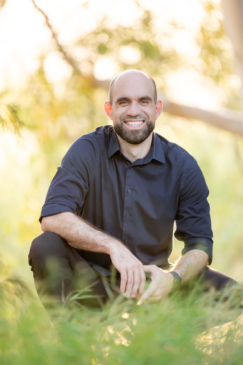 A black-shirted figure relaxes in golden sunlit grass during a casual outdoor photo session.