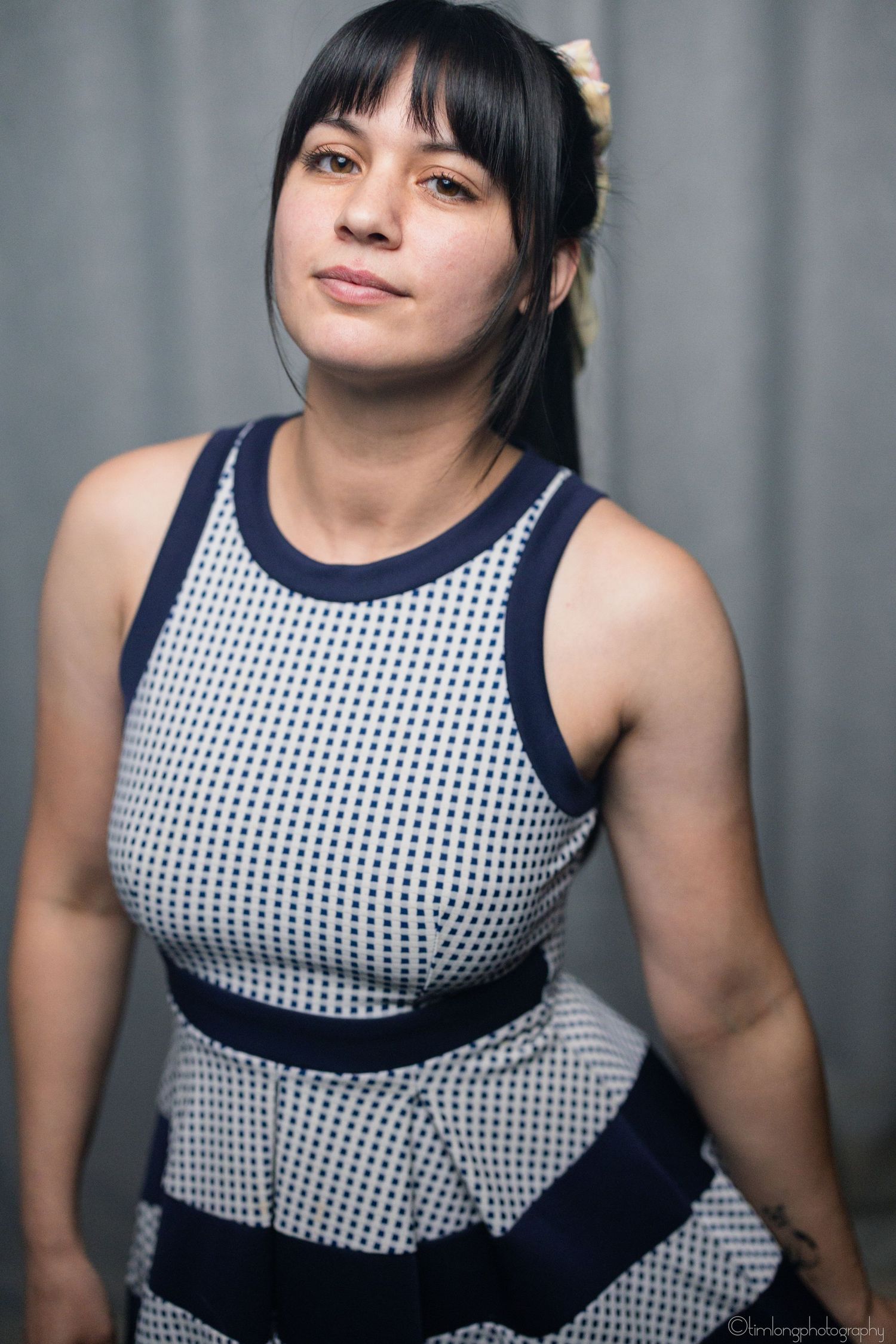 Woman wearing a black and white checkered sleeveless dress poses against a grey background.