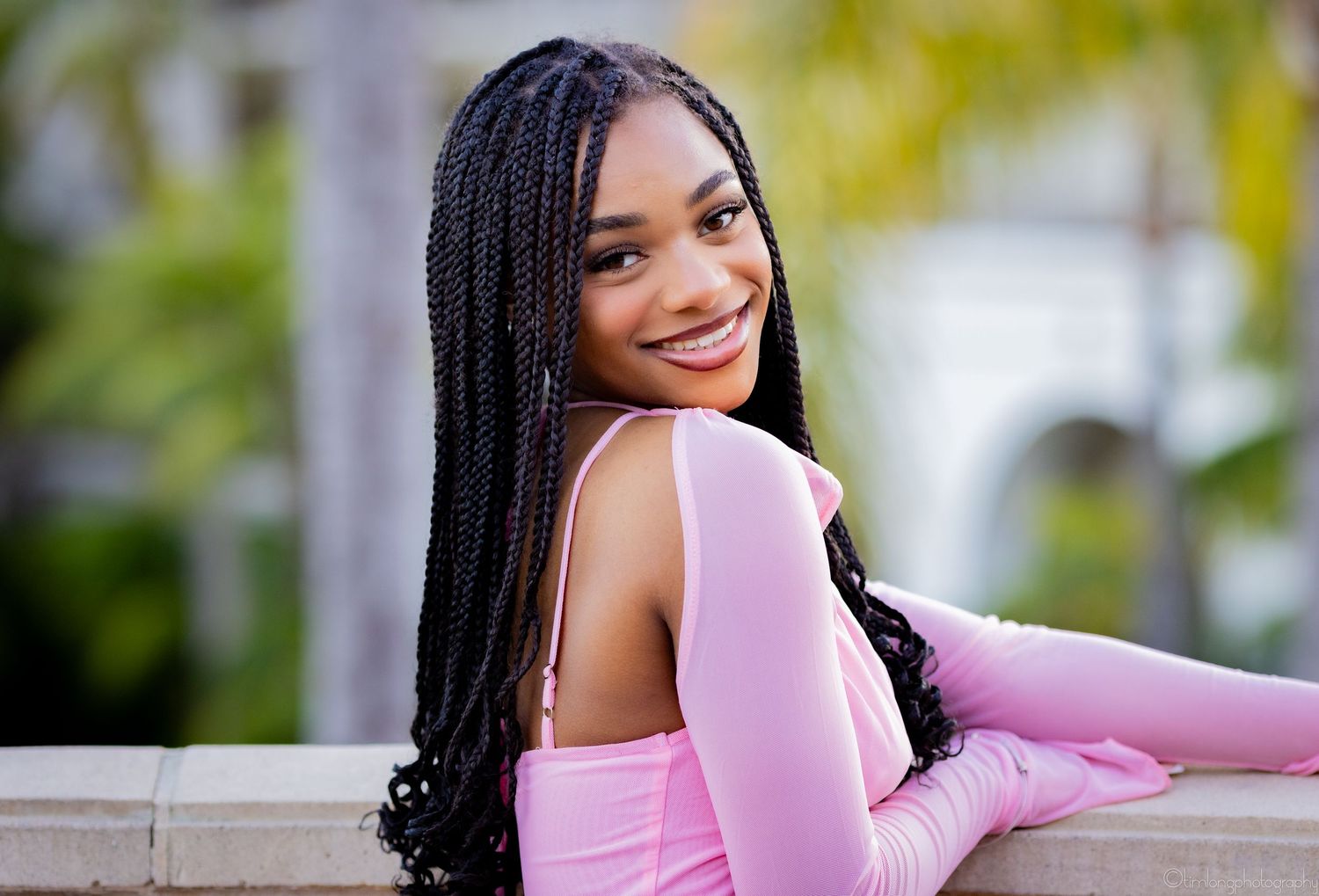 Portrait of person in pink long-sleeve dress posing outdoors with braided hairstyle.