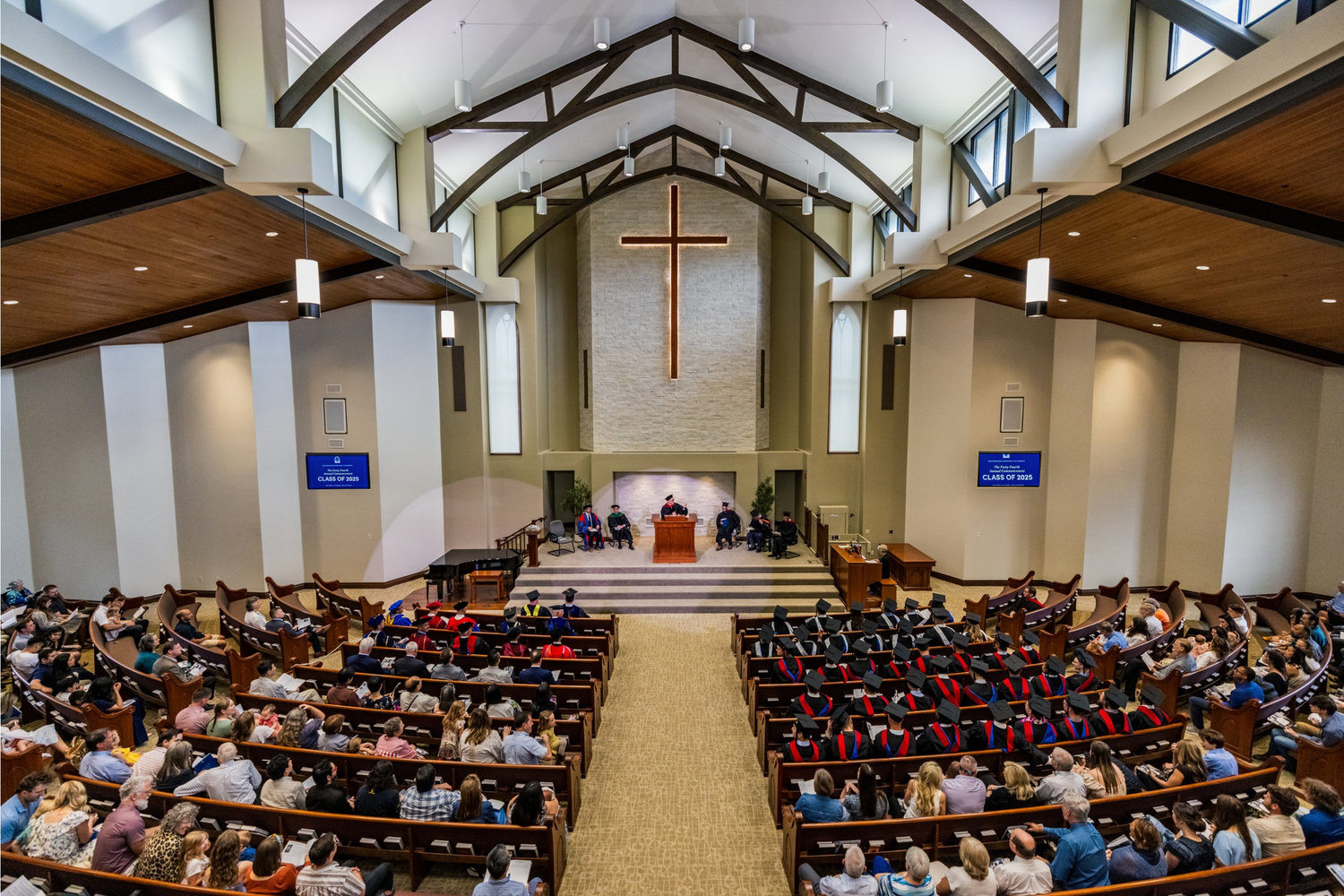 Large auditorium filled with seated attendees during a graduation or academic ceremony.