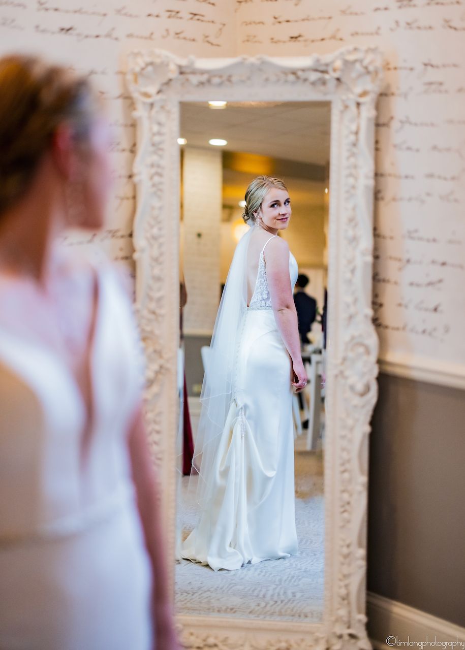Multiple reflections of a bride in white wedding dress captured through vintage mirrors in an elegant indoor setting.