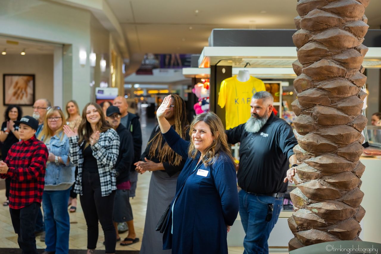 Crowd of attendees mingling in a mall setting with decorative palm trees.