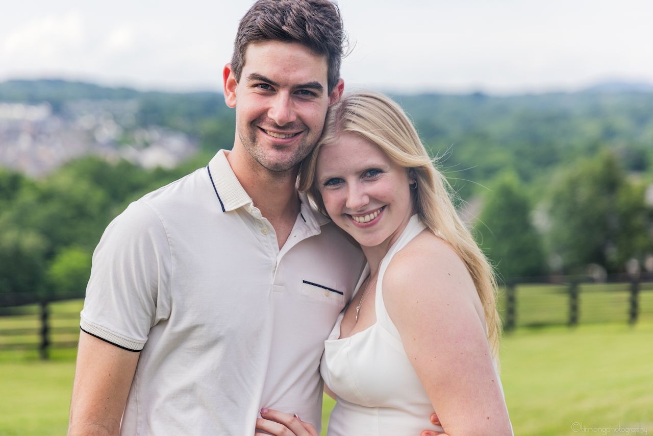 Happy couple smiling together outdoors with green hills in the background.