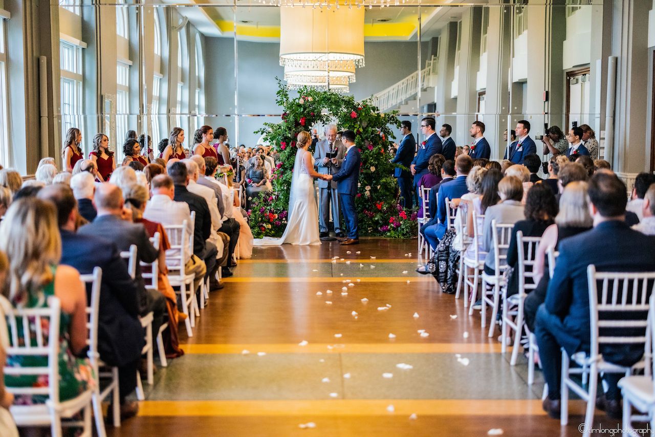 Long indoor ceremony space with white chairs and natural lighting.