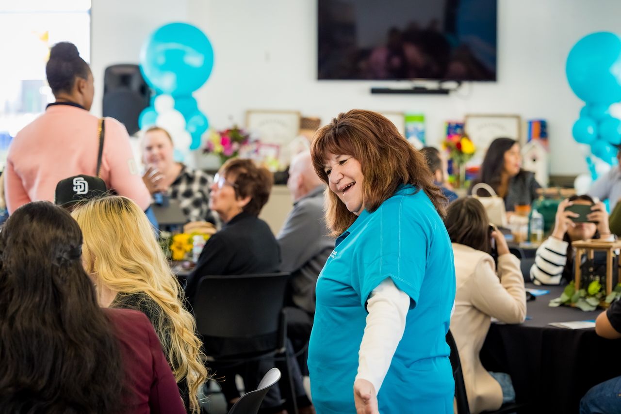 People celebrating at indoor event with turquoise balloons and festive atmosphere.