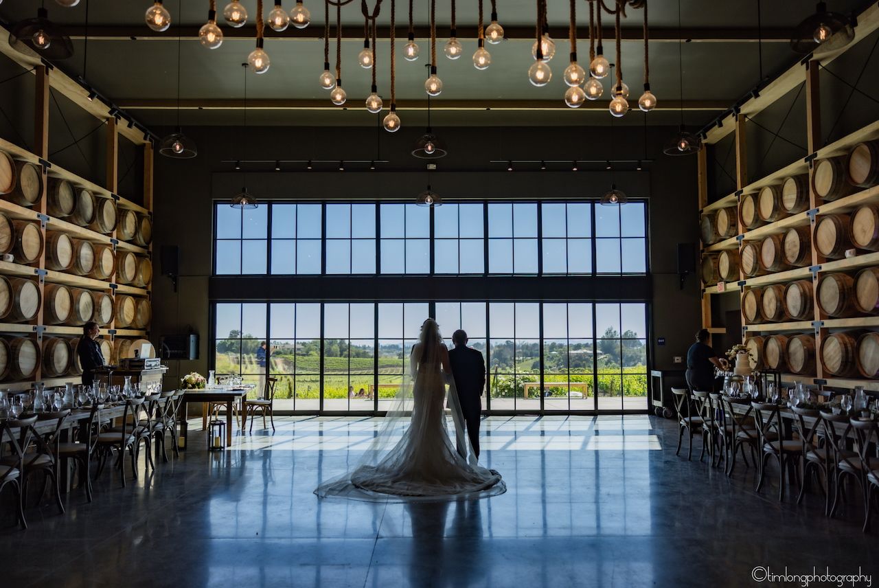 Dark industrial wedding venue with barrel storage and large windows overlooking scenic view.