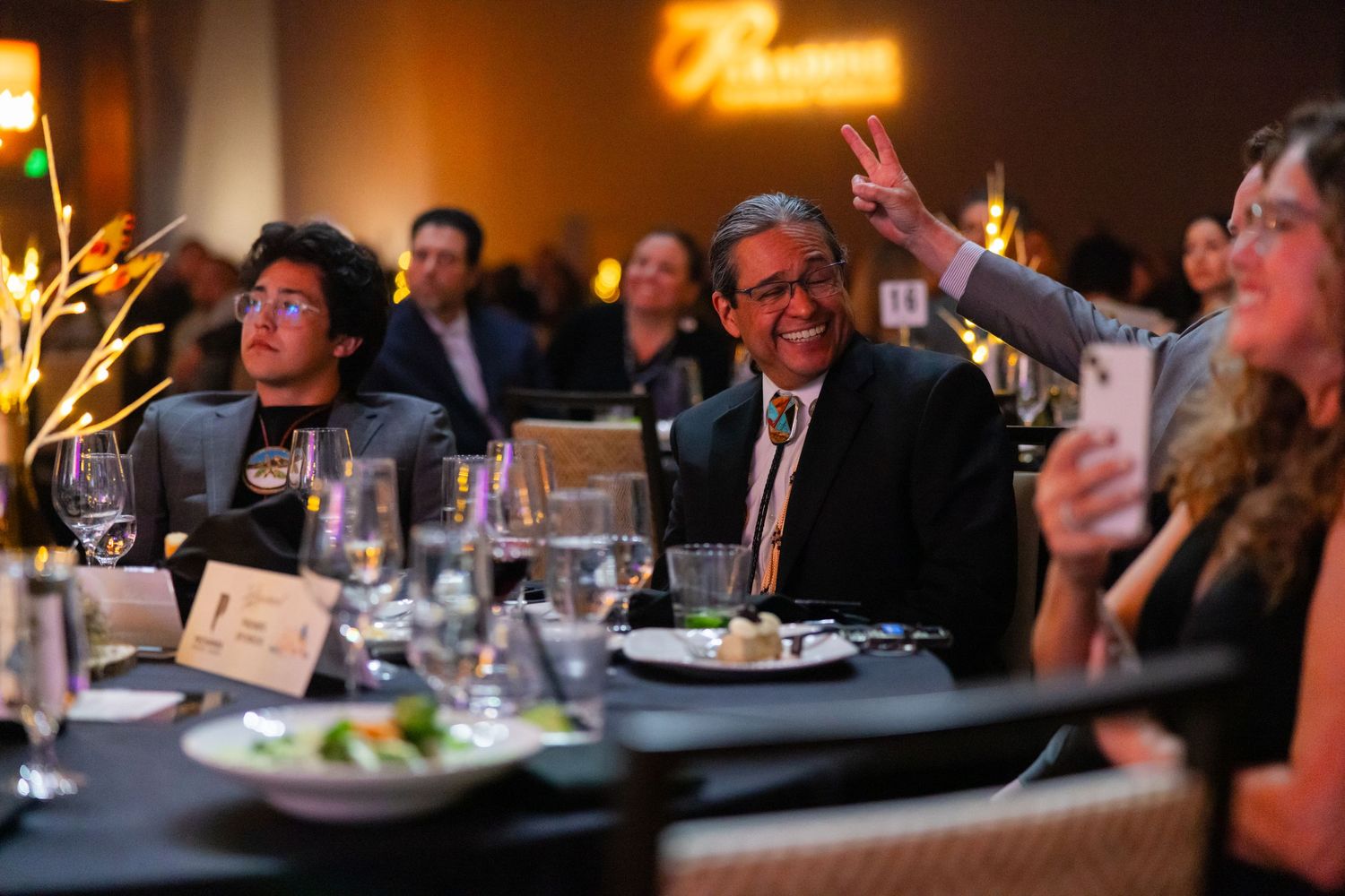 Audience members seated at dining tables in a dimly lit restaurant or event space.