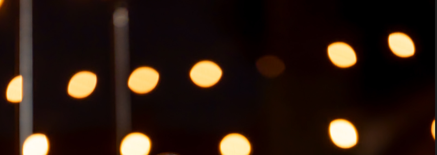 A lit candle display with soft bokeh lights in the dark background creating a warm, magical atmosphere.