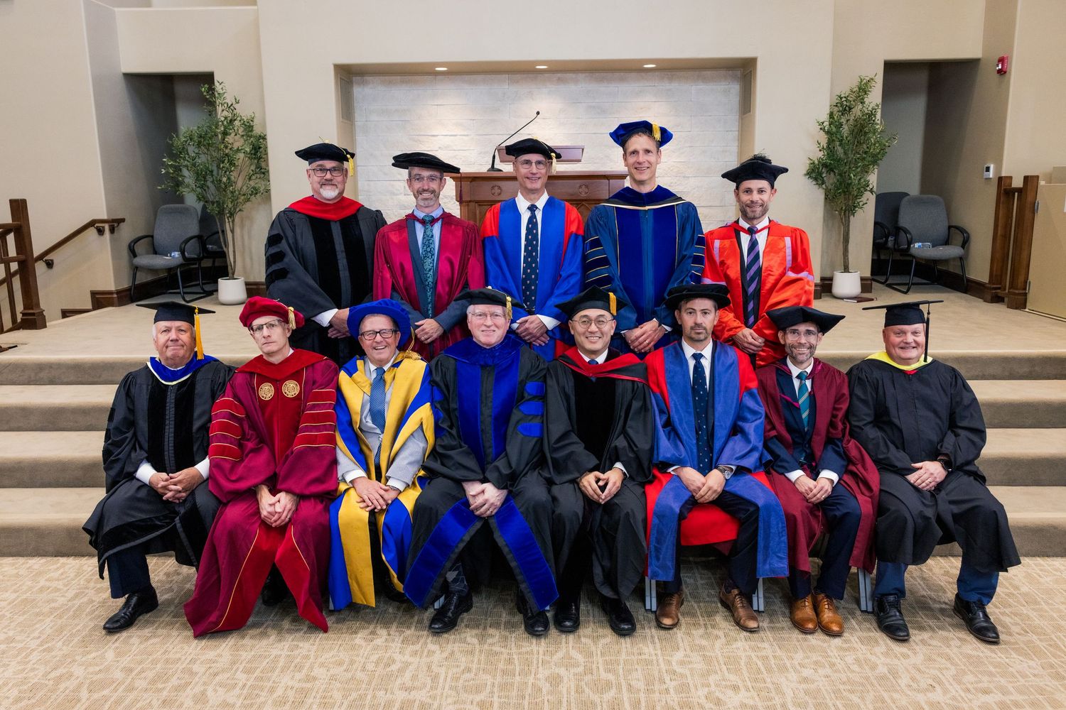 Faculty members in academic regalia and colorful hoods seated during graduation ceremony.