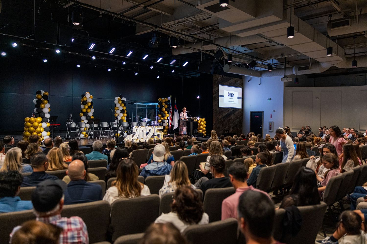 Large crowd seated in an auditorium during an indoor event with professional lighting and staging.