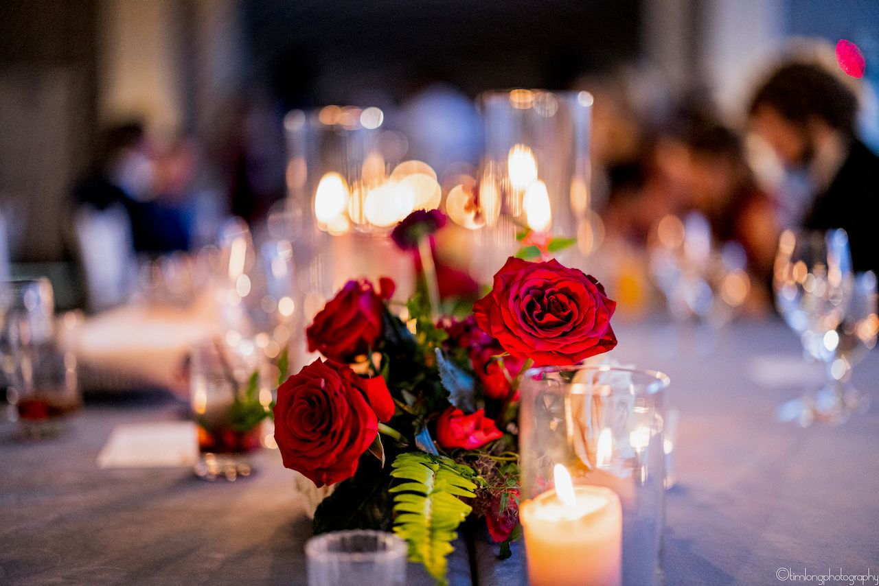 Red rose centerpieces and glowing candles decorate wedding reception tables.