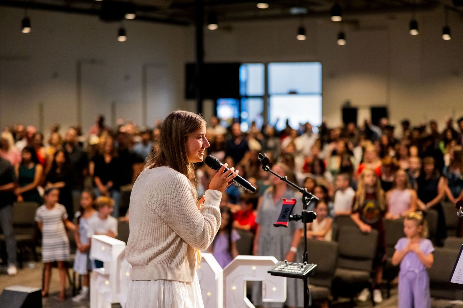 Speaker presenting to a packed audience in a modern conference venue with spotlights.